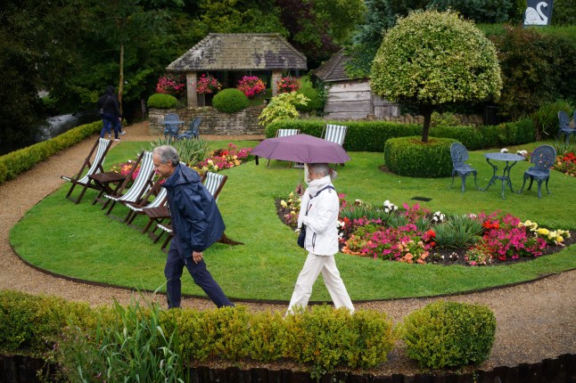 Visitors with umbrellas in the rainy weather at Bibury village in Gloucestershire. Picture date: Saturday August 24, 2024. PA Photo. Photo credit should read: Ben Birchall/PA Wire