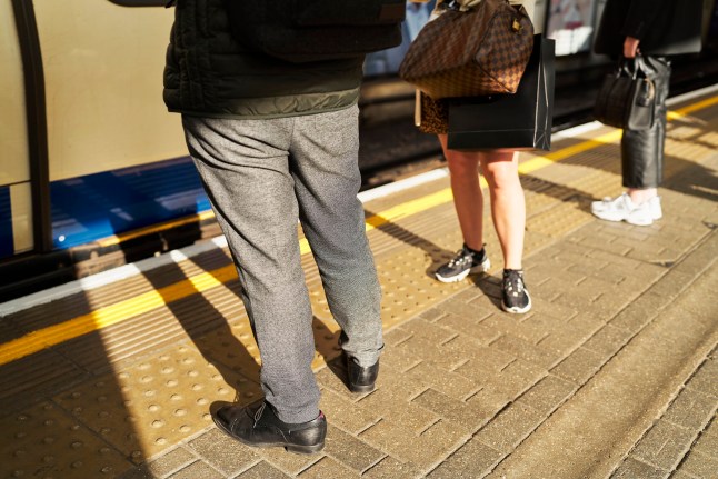 legs of people standing waiting at london train station waiting during daytime, rear view