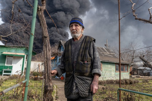 A local resident stands in a courtyard of his house while smoke rises from a fire following a strike