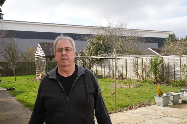 EAST ANGLIA NEWS SERVICE, tel 07767 413379 Dave Ward, 72, who is angry about the new warehouse built at the back of his garden in Nacton, Suffolk, pictured in his garden