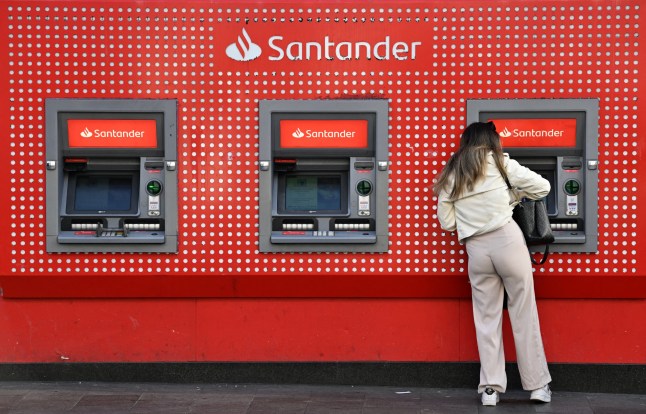 A person uses an ATM cash machine at a branch of a Santander bank in Liverpool, north west England, on March 19, 2025. Santander announced on Wednesday that it will close 95 of it's UK branches, also cutting staffing hours at a further 36 branches. (Photo by Paul ELLIS / AFP) (Photo by PAUL ELLIS/AFP via Getty Images)