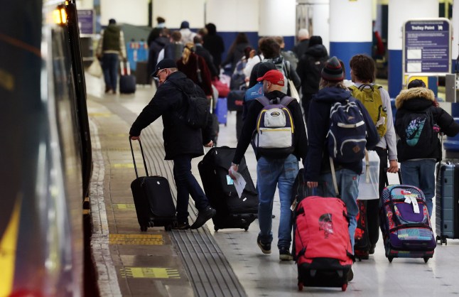 A group of rail passengers are seen pulling suitcases along a train station platform