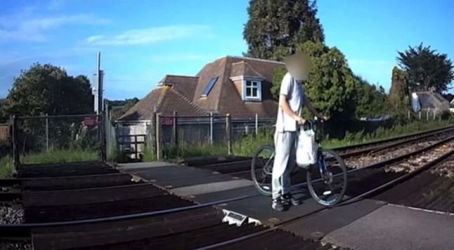 A cyclist standing on railway tracks before he is almost hit by a fast-moving passenger train on a railway level crossing in West Sussex.