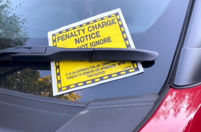 A car windscreen with a yellow PCN parking fine stuck under the wiper.