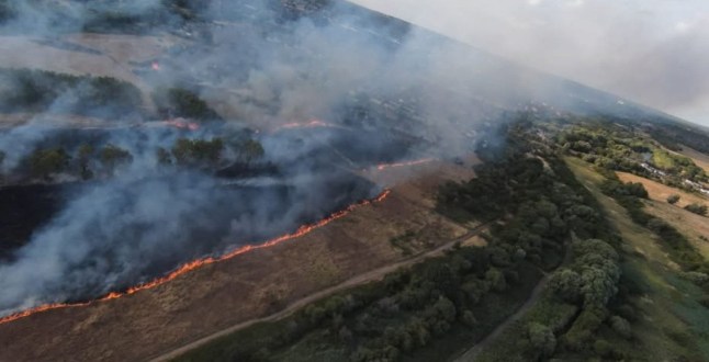 A huge grass fire has broken out behind Clemence Road in Dagenham, with around 125 firefighters and 20 fire engines battling the blaze, which has already scorched eight hectares of grassland, shrubbery, and woodland. The fire, which also involves fences and garden furniture, prompted emergency evacuations of nearby homes. Thick smoke can be seen across parts of Beam Valley Country Park, and residents are urged to keep all doors and windows shut. Firefighters from Multiple Stations Respond The London Fire Brigade???s Control Office began receiving over 75 calls about the fire just after 18:30. Crews from Dagenham, Hornchurch, Wennington, Romford, and other surrounding stations are on scene. A spokesperson confirmed: ???Firefighters are tackling a fire involving around eight hectares of grass, shrubland and trees. Nearby properties are being evacuated as a precaution.??? Public Safety Alert and Road Closures Emergency services have cordoned off roads in the RM10 area, with members of the public advised to avoid the scene entirely. The cause of the fire remains unknown at this stage, and investigations will begin once the fire is under control. Ongoing Coverage The incident comes amid extremely dry conditions during the UK???s heatwave, raising concerns of further wildfires in coming days. This is a developing emergency, and further updates will be provided throughout the evening.