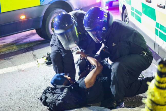 A major public order incident erupted in Epping on Thursday evening after a protest outside the Bell Hotel escalated into violent clashes, prompting the deployment of over 180 police officers from Essex Police, the Metropolitan Police, and Hertfordshire Constabulary. What began as a peaceful demonstration over the recent arrest of an Ethiopian asylum seeker accused of sexually assaulting a 14-year-old schoolgirl turned chaotic around 8pm, when officers issued a Section 39 dispersal order to the crowd gathered outside the hotel. Protesters reportedly refused to disperse, and some began hurling bricks, bottles, sticks, road signs, and cones at officers. Scenes quickly descended into street-level disorder, with injuries and property damage reported. Metropolitan Police Deployed in Riot Gear Specialist public order units from the Metropolitan Police Tactical Support Group (TSG) and the Commissioner???s Reserve were urgently deployed to support Essex officers already on the ground. Clad in full riot gear, officers formed shield lines and pushed back the crowd in a coordinated effort to regain control. At least two police vehicles ??? including an Essex Police van ??? were damaged during the melee. Several officers were struck by rocks and wooden poles during the confrontation. The exact number of injuries has not yet been confirmed. Multiple Arrests Made Essex Police have confirmed that multiple arrests were made on suspicion of violent disorder, assaulting emergency workers, and refusing to comply with dispersal orders. The area surrounding the Bell Hotel has now been cordoned off, and a large police presence is expected to remain overnight. Community Response Local residents watched in disbelief as the scene unfolded in the heart of their town. ???We were worried it would get worse, but once the reinforcements came, the police moved fast and got things under control,??? said one resident living near the hotel. The Bell Hotel has reportedly been used to house