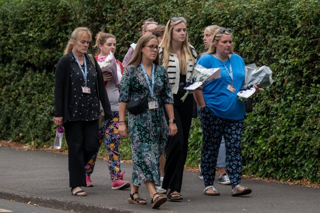 MINEHEAD, ENGLAND - JULY 18: A group approach Minehead Middle School with flowers on July 18, 2025 in Minehead, England. A child has been killed and 21 people injured in a coach crash carrying children back from a trip to the zoo. On Thursday afternoon, the coach flipped onto its roof and slid down a bank on a remote road near Exmoor in Somerset. (Photo by Matthew Horwood/Getty Images)
