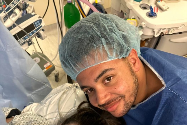 A man in a hospital cap and blue scrubs smiles
