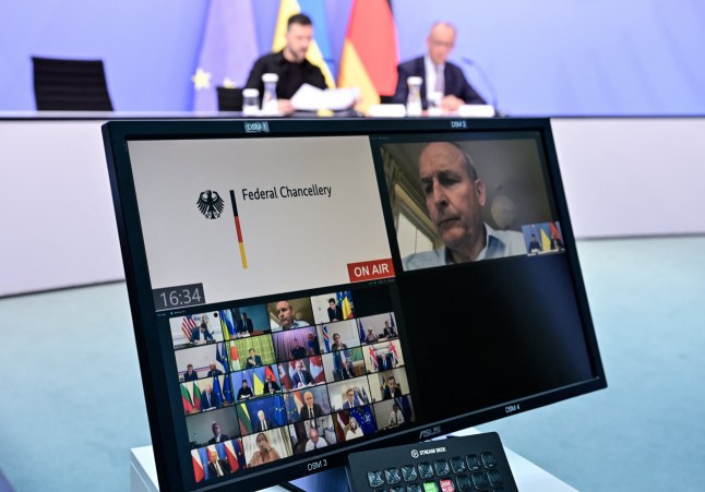A screen is seen in front of Ukrainian President Volodymyr Zelensky (back L) and German Chancellor Friedrich Merz (back R) attend a video conference of European leaders with the US President on the Ukraine war ahead of the summit between the US and Russian leaders, on August 13, 2025. European leaders will hold online talks with US President Donald Trump, hoping to convince him to respect Ukraine's interests when he discusses the war with Putin in Alaska on Friday. (Photo by John MACDOUGALL / POOL / AFP) (Photo by JOHN MACDOUGALL/POOL/AFP via Getty Images)