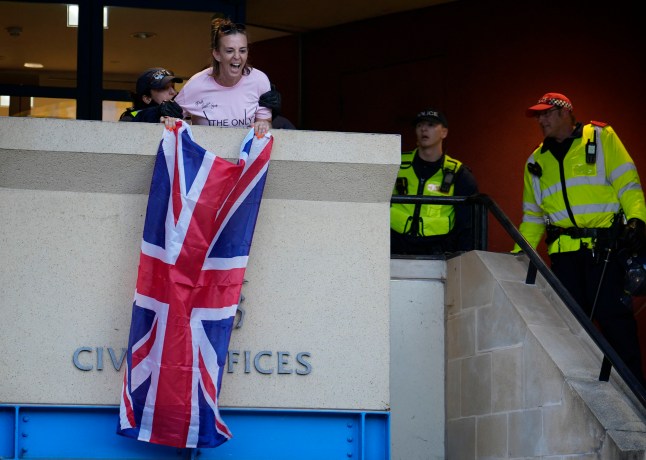 A protester hangs a Union flag from the civic offices before being detained by police, as protesters march in Epping, Essex after a temporary injunction that would have blocked asylum seekers from being housed at the Bell Hotel, was overturned at the Court of Appeal. Picture date: Sunday August 31, 2025. PA Photo. Photo credit should read: Jordan Pettitt/PA Wire