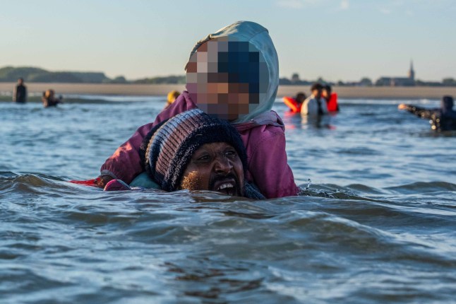 GRAVELINES, FRANCE - AUGUST 25: A man struggles in deep water as he carries a young child on his shoulders to try and board a migrant dinghy into the English Channel on August 25, 2025 in Gravelines, France. Migrant crossings by boat have caused much controversy in the UK, with far-right groups organising demonstrations outside hotels housing migrants across the country over the summer. As of late August 2025, more than 28,000 migrants have crossed the English Channel in small boats this year. (Photo by Carl Court/Getty Images)