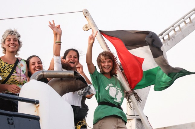 Greta Thunberg and a crew member flash victory signs from their ship, part of the Global Sumud Flotilla aiming to reach Gaza and break Israel's naval blockade, as they sail off Crete island, Greece, September 25, 2025. REUTERS/Stefanos Rapanis