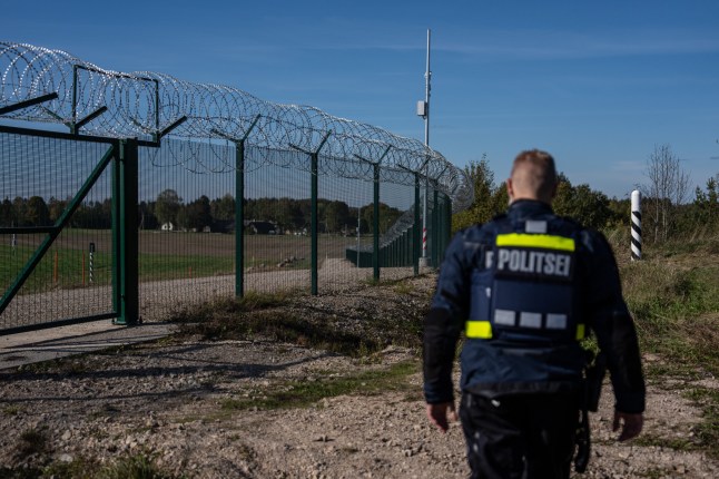 A border police officer walks along the gate at the border between Estonia and Russia