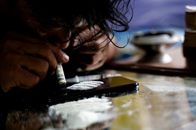 Drug addict man sniffing cocaine lines on smart phone with rolled banknote. drug abuse concept.