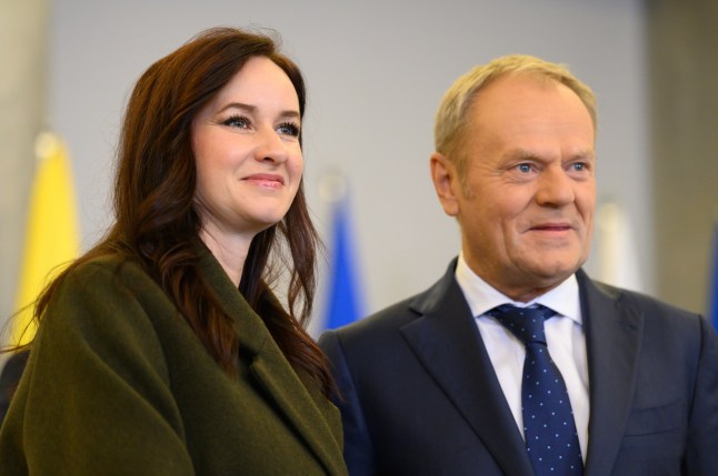 Polish Prime Minister Donald Tusk (right) with Lithuania's PM Inga Ruginiene (left) both standing in front of flags that are blurred in the background