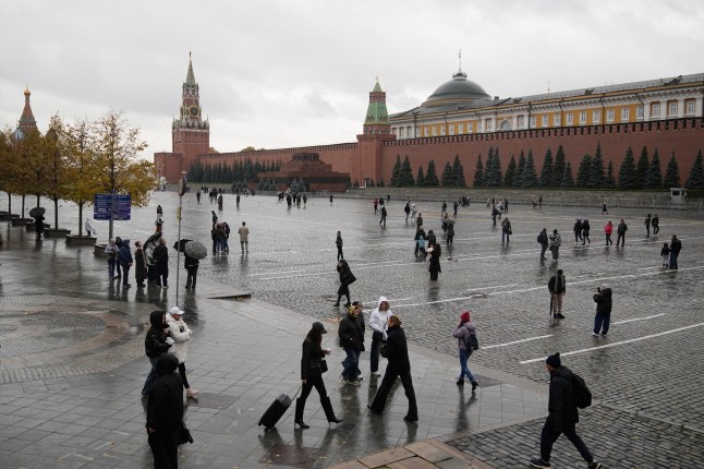 People walk under the rain through Red Square with the Spasskaya Tower and the Kremlin Wall in the background in Moscow, Friday, Oct. 17, 2025. (AP Photo/Pavel Bednyakov)