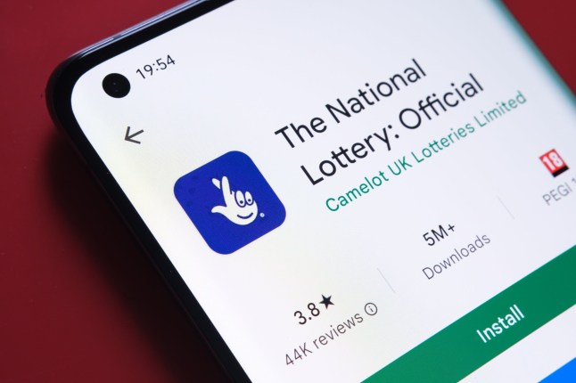 The national Lottery app seen in Google Play Store on the smartphone screen placed on red background. Close up photo with selective focus. Stafford, United Kingdom, August 2, 2022.; Shutterstock ID 2191607641; purchase_order: -; job: -; client: -; other: