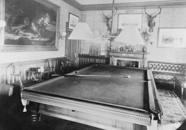 Photograph of the Billiard Room at York Cottage, Sandringham, October 1897 A photograph of the interior of the Billard Room at York Cottage on the Sandringham Estate. The photograph shows the billiard table in the centre of the room, cues stored at the back of the room, mounted stag heads on the back wall and a hunting scene painting (RCIN 402444) to the left of the room. (Picture: Royal Collection Trust)