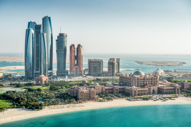 Sea and skyscrapers in Abu Dhabi alongside a beach and turqouise blue waters.