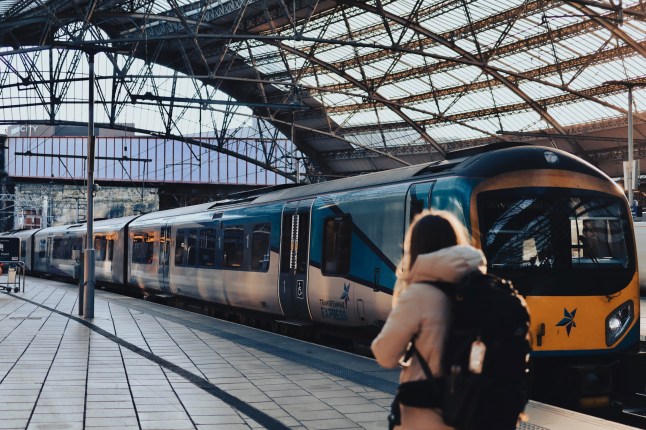Liverpool Lime Street Station, the main railway station in Liverpool, UK, is captured in the golden light as a TransPennine Express train prepares for departure. A traveler with a backpack walks along the platform, emphasizing the station's role as a key transport hub connecting northern England. The intricate iron and glass architecture of the station's roof highlights its historical significance and modern functionality.