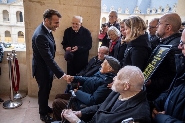 Henri Hagenbach, center behind, watches French President Emmanuel Macron greeting World War II veterans after the inauguration of a plaque in memory of the soldiers from the Alsace and Moselle regions, at the Invalides monument