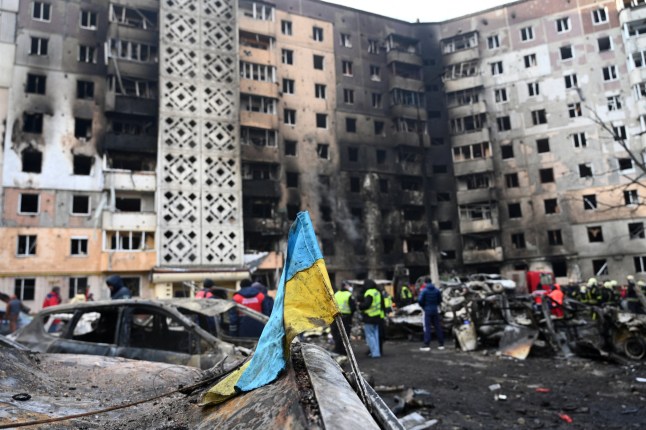 A Ukrainian flag is seen attached to a burned car at the site of a heavily damaged residential building