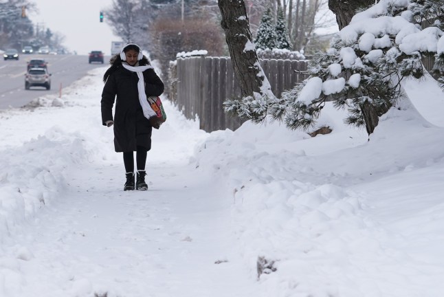 A pedestrian walks on a snow-covered sidewalk during a cold day in Northbrook, Ill., Tuesday, Dec. 2, 2025. (AP Photo/Nam Y. Huh)