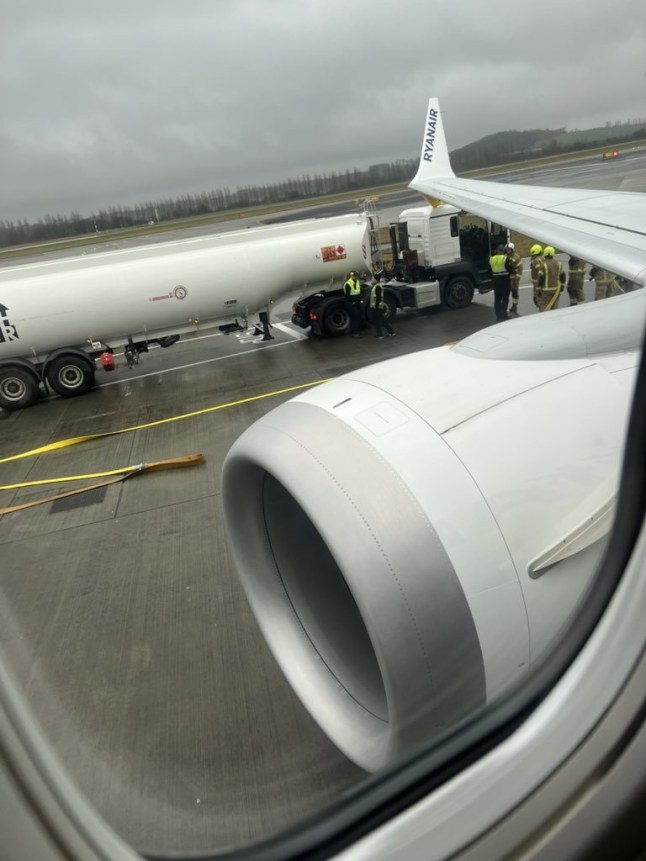 A picture taken from the cabin window of an Ryanair plane at Edinburgh Airport with fuel tanker on the background.