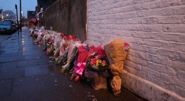 Floral tributes rest against a wall as police officers distribute leaflets to members of the public appealing for witnesses to come forward to assist with inquiries into the murder of Tanesha Melbourne-Blake in Chalgrove Road, Tottenham.