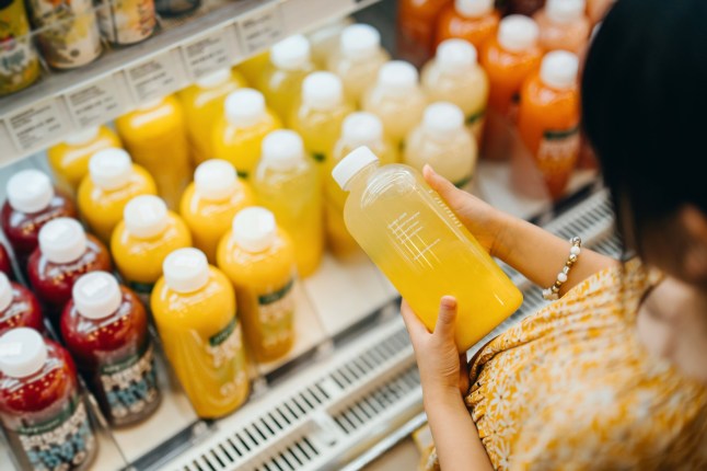 Asian girl grocery shopping in supermarket. She is choosing fresh fruit juice along the beverage aisle, reading the nutrition label and checking ingredients on the bottle. Making a healthier food choice and balanced diet. Healthy eating lifestyle