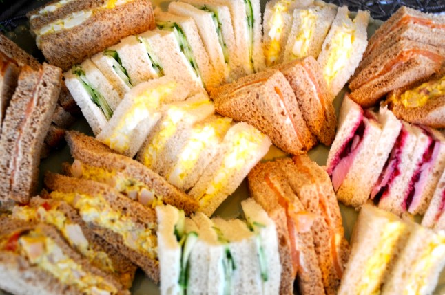 A variety of homemade finger sandwiches fills a large platter. White bread, brown bread, curried egg, cucumber, coronation chicken & Turkey with cranberry fill the plate