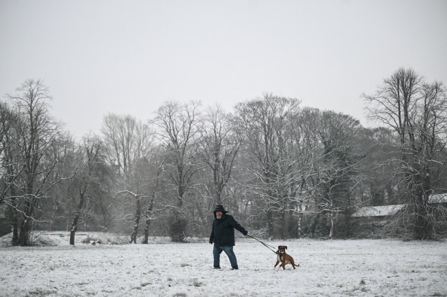 A man walks his dog across a snow-covered field in the town of Glossop, Derbyshire, northern England on January 6, 2026. The UK's Met Office issued fresh weather warnings for January 5-6 for snow and ice for Scotland, Northern Ireland and parts of northern England and said cold weather health alerts for all English regions would remain in place until January 9. (Photo by Oli SCARFF / AFP via Getty Images)