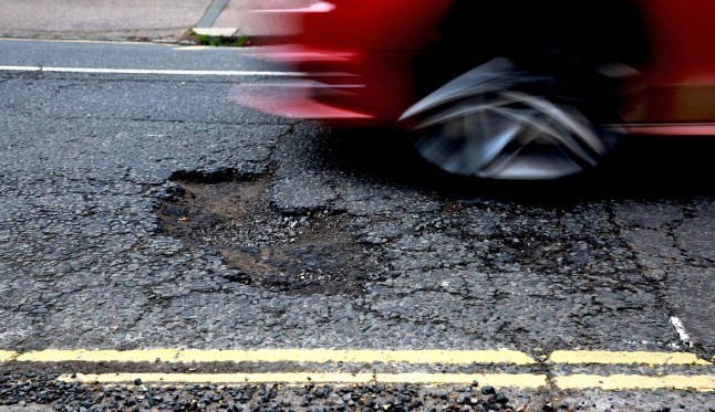 The front wheel of a moving car about to enter a pot hole in the street